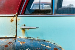 Vintage car door with rust and cracked faded paint around the handle