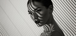 Black and white portrait of a beautiful young girl with a shadow pattern on the face and body in the form of stripes.fashion, beauty, makeup, cosmetics, beauty salon, style, personal care, posture.