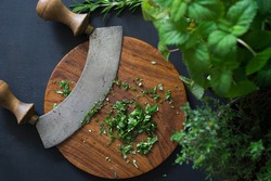 Aromatic herbs chopped with mezzaluna knife on wooden cutting board