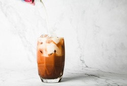 pour milk and make Iced cocoa in clear glass on marble, copy space for your text