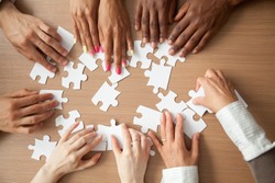 Hands of diverse people assembling jigsaw puzzle, african and caucasian team put pieces together searching for right match, help support in teamwork to find common solution concept, top close up view