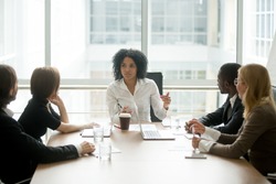 Black female boss leading corporate multiracial team meeting talking to diverse businesspeople, african american woman executive discussing project plan at group multi-ethnic briefing in boardroom