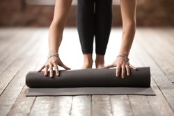 Young woman rolling black fitness or yoga mat before or after sport practice, working out at home in living room or in yoga studio. Healthy habits, keep fit, weight loss concepts. Close up view photo
