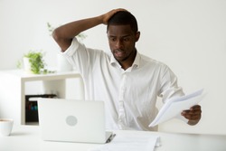 Confused african-american businessman having problem with documents looking at laptop at work, frustrated black employee stressed by mistake or unexpected computer error crash, forgot about deadline
