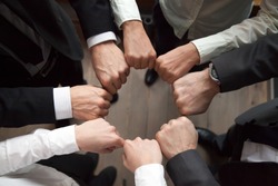 Business team or partners put fists in circle as concept of motivating engaging teambuilding activity, reliable support, help in cooperation, trust unity in collaboration teamwork, close up top view