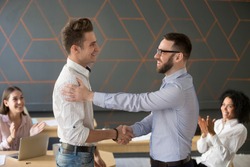 Team leader handshaking employee congratulating with professional achievement or career promotion, thanking for good project result while team supporting applauding, appreciation recognition concept