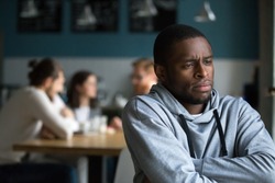 Frustrated excluded outstand african american man suffers from bullying or racial discrimination having no friends sitting alone in cafe, sad depressed black guy upset being rejected by white people