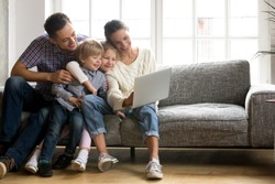 Happy family with little kids enjoying using application on laptop together, smiling parents spending time with children son and daughter having fun watching video or doing internet shopping at home