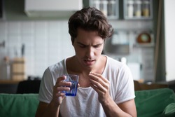 Millennial man taking antibiotic antidepressant painkiller pill medication to relieve pain at home, young guy feeling sick ill suffering from headache, stress or flu, emergency treatment concept