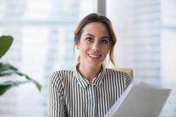 Portrait of smiling millennial businesswoman holding documents looking at camera, headshot of happy woman worker or female ceo posing with paperwork making picture at corporate close up photoshoot.