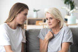 Concerned aged mother and adult daughter sit on couch having serious conversation, young woman talk with worried elderly mom, listen to her sharing problems or concerns, help dealing with depression