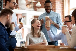 Happy diverse colleagues have fun at lunch break in office, smiling multiracial employees laugh and talk eating pizza and drinking coffee, excited workers celebrate shared win ordering takeaway food