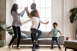 Happy african american family and funny active children having fun dancing together at new home, cheerful black parents and two kids enjoying moving to music spending weekend time in living room