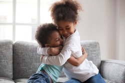 Cute happy african american siblings hugging cuddling feeling love and connection, smiling mixed race kid girl sister embracing little boy brother sitting on couch, 2 children good relationships