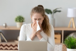 Ill young woman caught cold sneezing in tissue at home or in office, sick allergic girl blowing wiping running nose got flu rhinitis sinusitis coughing, having seasonal allergy symptoms at workplace