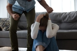 Frightened scared young defenseless woman victim hiding from aggressive man suffer from physical abuse, abusive husband threaten beat upset crying wife with fists, fear of domestic violence concept