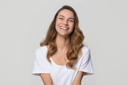 Happy cheerful young woman with beautiful face, teeth and hair laughing looking at camera on white light background, smiling pretty girl model having fun isolated on blank grey studio wall, portrait