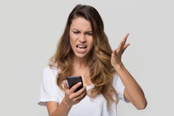 Annoyed angry young woman mad about spam message stuck phone looking at smartphone isolated on blank studio background, furious teen girl having problem with cellphone irritated by broken mobile