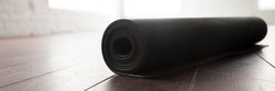 Horizontal photo close up black yoga fitness floor mat in a roll inside of gym studio. Active lifestyle healthy habit sport fitness concept. Banner for website header design with copyspace for text