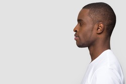 Millennial african american man standing in profile isolated on blank white grey studio background, confident black guy looking forward at copy space thinking of future leadership, side view portrait