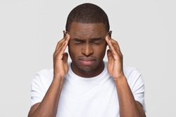 Stressed young african american man feel pain having terrible strong headache concept, tired upset black guy massaging temples suffering from migraine isolated on white grey studio blank background