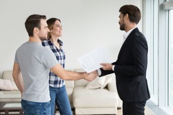 Realtor or landlord handshaking couple buyers tenants make real estate deal holding rental agreement or sale purchase contract, agent and clients shake hands welcoming renters in new home apartment