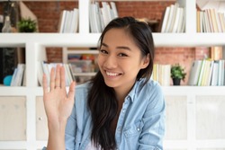 Happy asian teen girl student making video call to distant friend looking at camera waving hand, smiling female vlogger saying hello to webcam making video blog recording vlog, portrait