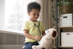 Cute little toddler african american boy playing funny game as doctor holding stethoscope listening to toy, mixed race black preschool child kid pretending nurse treating fluffy patient at home