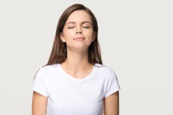 Happy calm teen girl enjoying good smell or pleasant fragrance, serene mindful young woman taking deep breath feel no stress free inhaling fresh air relaxing isolated on white grey studio background