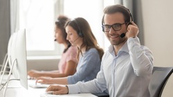 Smiling male call center operator in wireless headset with microphone looking at camera at workplace, businessman agent telemarketer work in customer service helpline support team office, portrait