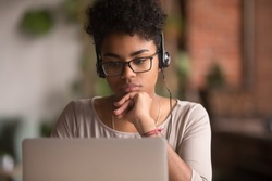 Focused african american girl student wearing headphones looking at laptop watching online webinar training course, serious mixed race woman learning english language on computer, internet e-learning