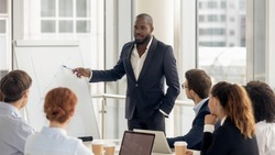African american conference speaker coach talk to audience give presentation on flipchart to employees group, black trainer manager speaking training diverse corporate team at office meeting seminar