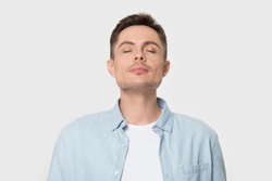Calm young Caucasian male isolated on grey studio background enjoy pleasant smell or fragrance, relaxed European man in shirt breath deep, feel mindful inhaling fresh air. Stress free concept