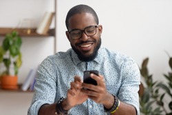 Happy african american businessman using phone mobile corporate apps at workplace texting sms, smiling black man looking at smartphone browsing internet, office technology and digital communication