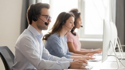 Service phone operators use headset and computer, focus on man side view answers incoming telephone calls directing to appropriate department, takes messages from clients, assistance distantly concept