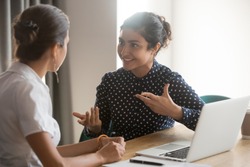 Excited multiethnic female employees discuss work issues sitting at office table, smiling diverse women workers or colleagues engaged in brainstorming talk chatting, explain ideas at workplace
