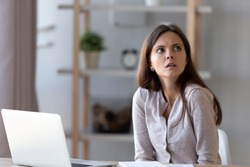 Confused young woman sit at office home desk working at laptop look at clock realizing missing deadline, frustrated disappointed girl feel puzzled late for appointment, forget meeting or gathering