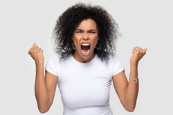 African woman in white t-shirt screaming make fists feels mad open mouth shouting aloud look at camera isolated on grey blank studio head shot. Negative emotions crazy face furious girl concept image
