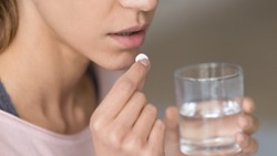 Close up image woman holding round pill and glass of still water taking painkiller to relieve painful feelings migraine headache, antidepressant or antibiotic medication, emergency treatment concept