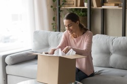 Happy woman sitting on couch at home opening carton box received parcel package from relatives or shopper make order internet website satisfied client, easy and fast service commerce delivery concept