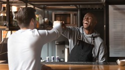 Labor Costs - 7 Best Ways To Manage The Labor Costs for a Restaurant 5 Laughing African American barista fists bumping with customer in cafe, excited bartender wearing apron standing behind bar counter, greeting friend or regular customer in coffeehouse
