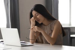 Overworked stressed asian business woman employee holding glasses feeling pain in dry eye strain or headache suffer from bad blurry weak vision tired of computer work syndrome, sight problem concept