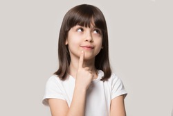 Thoughtful little girl brown-haired child touch chin with finger thinking or considering, pensive lovely daughter making decision imagining idea posing isolated on beige studio background