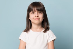 Adorable six years old girl in white t-shirt isolated on blue studio background, pretty brown-haired fringe hairstyle european appearance child pose indoor smiling look at camera, generation Z concept