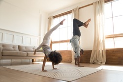 Sporty active african american family father and kid daughter doing handstand at home, healthy parent black dad with cute little child girl enjoy leisure gymnastic activity playing together at home