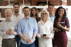 Happy diverse professional business team stand in office looking at camera, smiling young and old multiracial workers staff group pose together as human resource, corporate equality concept, portrait