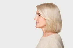 Mature woman profile view studio portrait isolated on gray background. Blond female with good styling, hairstyle side view headshot. Old lady looking to left, copyspace mockup template, blank space