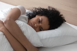 Sad depressed african american young woman hugging pillow lying in bed alone, upset frustrated black lady feeling lonely anxious suffer from insomnia trying to sleep thinking of problem in bedroom