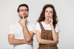 Thinking millennial couple pose isolated on grey studio background, pretty girl handsome guy wearing glasses touch chin posture of indecision doubting feelings anxiety, deliberating brain work concept