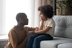 Loving african American father talk with upset preschooler daughter helping with problem, caring black young dad speak with sad girl child holding caressing hand, show support and understanding